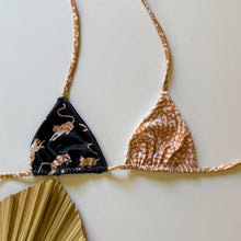 Load image into Gallery viewer, Two triangle bikini tops, one in a black and gold pattern and the other in a beige and brown pattern, displayed on a flat surface with a palm leaf fan in the background.