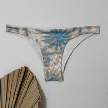 Load image into Gallery viewer, A multicolored swimsuit bottom with geometric patterns displayed against a white background with a decorative object to the left.