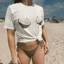 Load image into Gallery viewer, Person wearing a white t-shirt with coconut design on a beach
